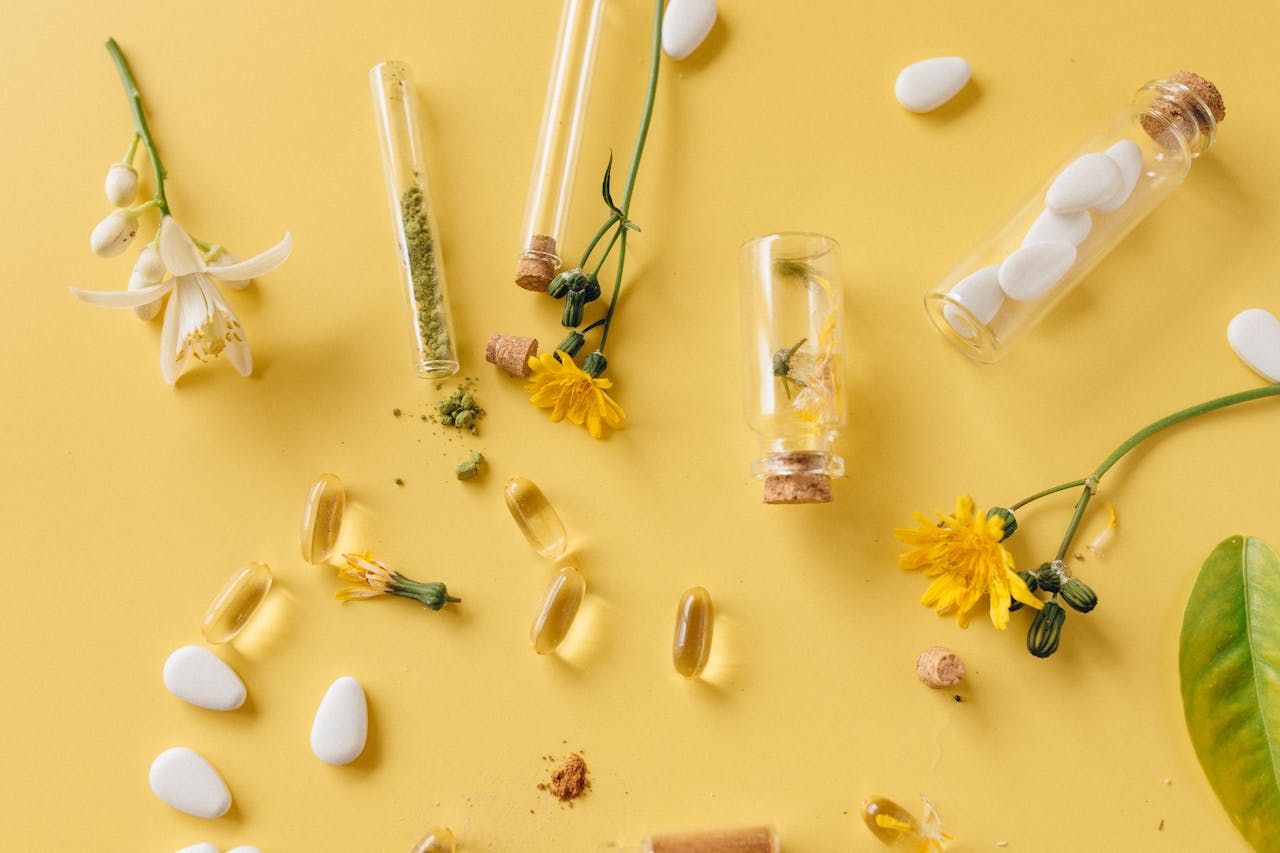 An arrangement of medicinal herbs, pills, and flowers on a vibrant yellow surface, highlighting natural healthcare.